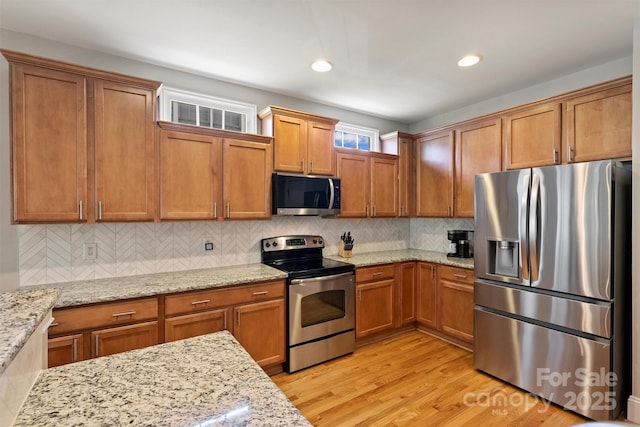 kitchen featuring light stone counters, stainless steel appliances, decorative backsplash, brown cabinetry, and light wood-type flooring