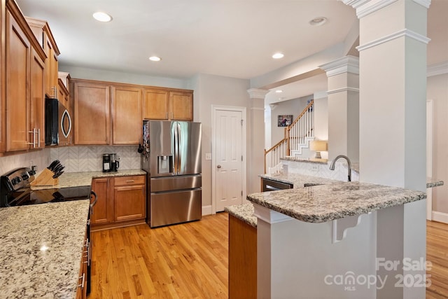 kitchen featuring light wood-style floors, appliances with stainless steel finishes, brown cabinets, a kitchen bar, and decorative columns