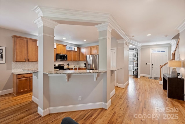 kitchen with light wood finished floors, light stone counters, a breakfast bar, stainless steel appliances, and ornate columns