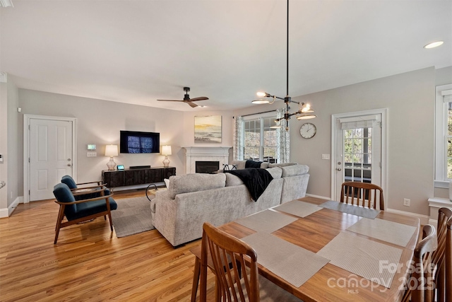 dining area with a fireplace, recessed lighting, light wood-style flooring, baseboards, and ceiling fan with notable chandelier