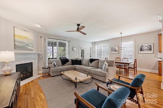 living room featuring baseboards, a fireplace with flush hearth, a wealth of natural light, and light wood-style floors