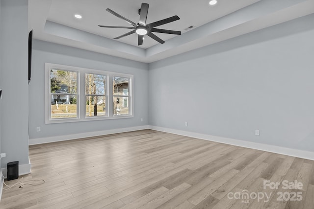 unfurnished living room with light wood-style floors, recessed lighting, a raised ceiling, and baseboards