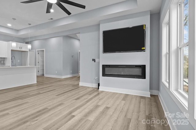 unfurnished living room with a glass covered fireplace, baseboards, a sink, and light wood finished floors