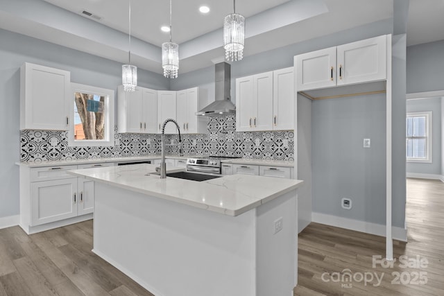 kitchen with a tray ceiling, white cabinetry, a sink, and wall chimney exhaust hood