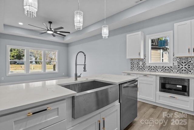 kitchen featuring dishwasher, light wood-style flooring, a tray ceiling, white cabinetry, and a sink