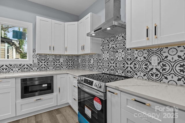 kitchen featuring white cabinets, decorative backsplash, electric stove, light stone countertops, and wall chimney range hood