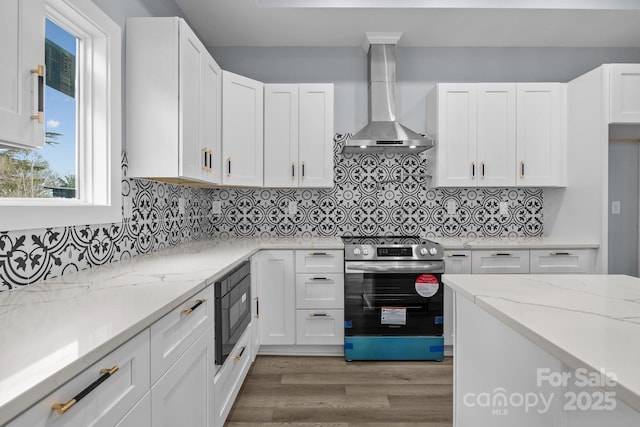 kitchen with black microwave, wall chimney exhaust hood, stainless steel range with electric stovetop, and white cabinets