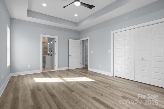 unfurnished bedroom with baseboards, a raised ceiling, and wood finished floors