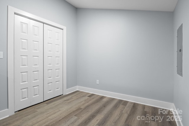 unfurnished bedroom with electric panel, a closet, baseboards, and wood finished floors