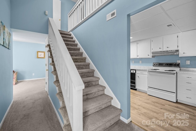 stairs with visible vents, a drop ceiling, baseboards, and wood finished floors