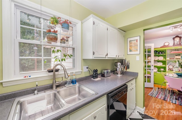 kitchen with black dishwasher, dark countertops, white cabinetry, a sink, and wood finished floors