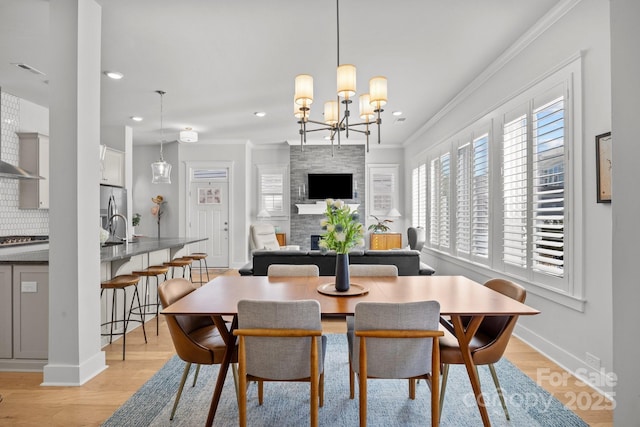 dining space with light wood-type flooring, a large fireplace, crown molding, baseboards, and a chandelier