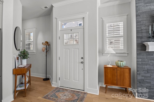 entrance foyer featuring visible vents, baseboards, crown molding, and light wood finished floors