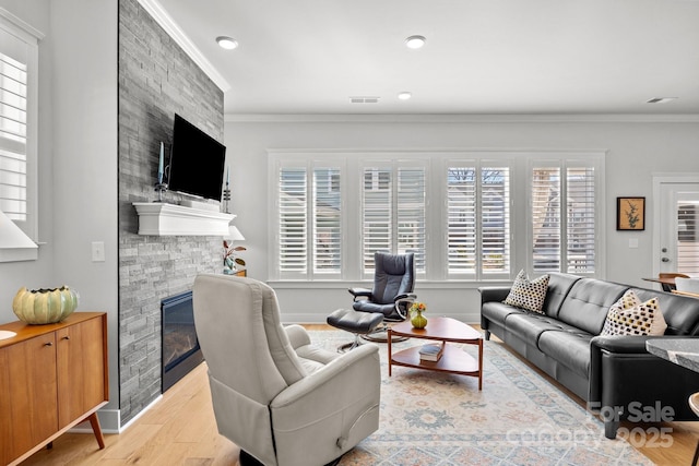 living room featuring wood finished floors, visible vents, baseboards, a fireplace, and crown molding