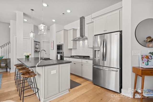 kitchen featuring visible vents, light wood-style floors, stainless steel appliances, wall chimney exhaust hood, and a sink