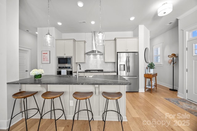 kitchen with a sink, decorative backsplash, appliances with stainless steel finishes, a kitchen bar, and wall chimney range hood