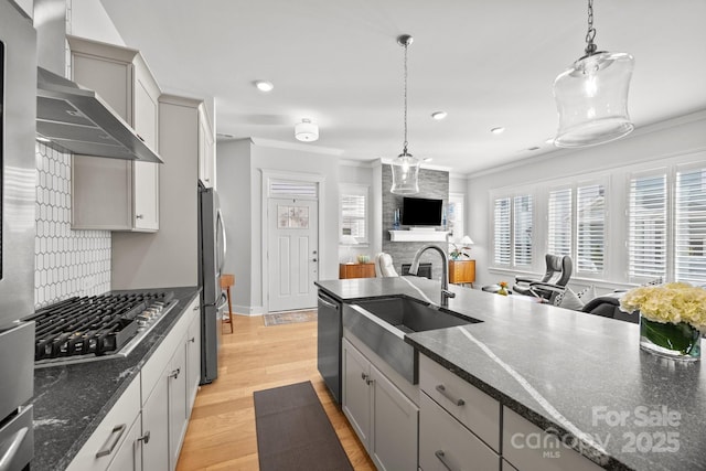 kitchen featuring stainless steel appliances, crown molding, wall chimney range hood, and a sink