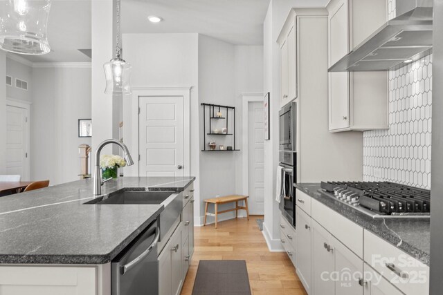 kitchen featuring visible vents, a sink, stainless steel appliances, light wood-style floors, and wall chimney range hood