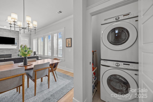 washroom featuring visible vents, stacked washing maching and dryer, an inviting chandelier, laundry area, and crown molding