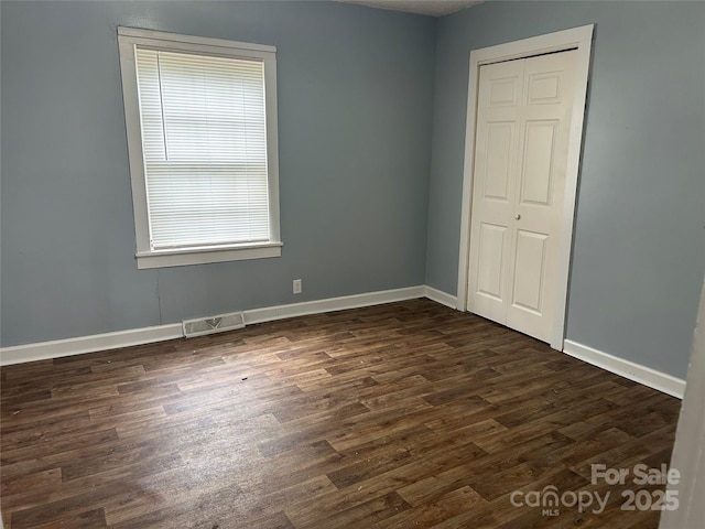 unfurnished room featuring baseboards, visible vents, and dark wood finished floors