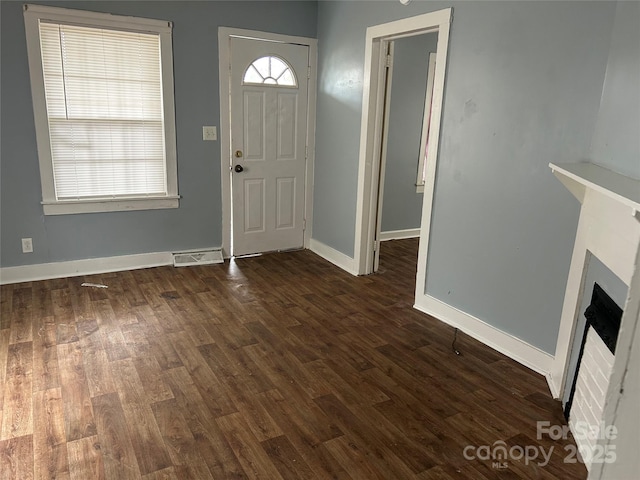 foyer entrance with baseboards, a fireplace, visible vents, and dark wood-style flooring