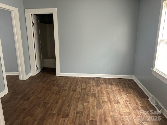 unfurnished bedroom with dark wood-style flooring, visible vents, and baseboards