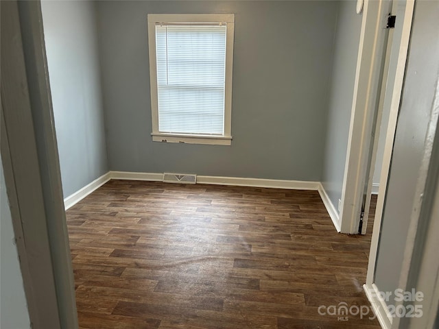 unfurnished room with baseboards, visible vents, and dark wood-type flooring