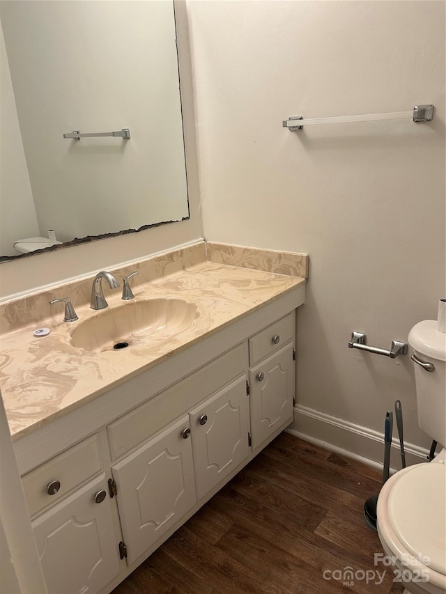 half bathroom with baseboards, vanity, toilet, and wood finished floors