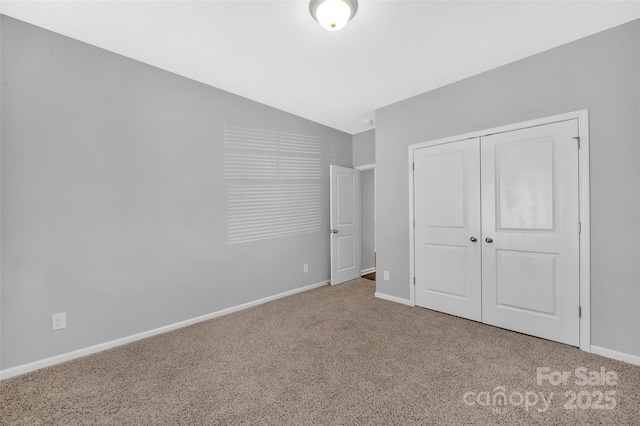 unfurnished bedroom featuring carpet, a closet, vaulted ceiling, and baseboards