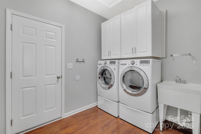 clothes washing area with cabinet space, a sink, separate washer and dryer, wood finished floors, and baseboards