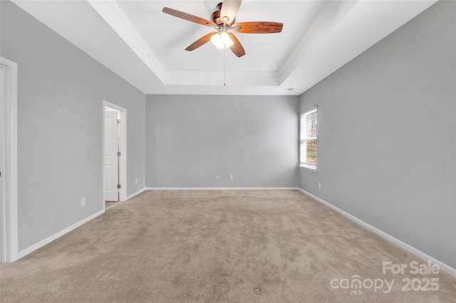 carpeted empty room with a raised ceiling, a ceiling fan, and baseboards