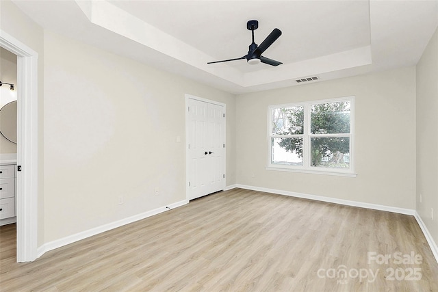 unfurnished bedroom featuring visible vents, light wood-type flooring, and a raised ceiling