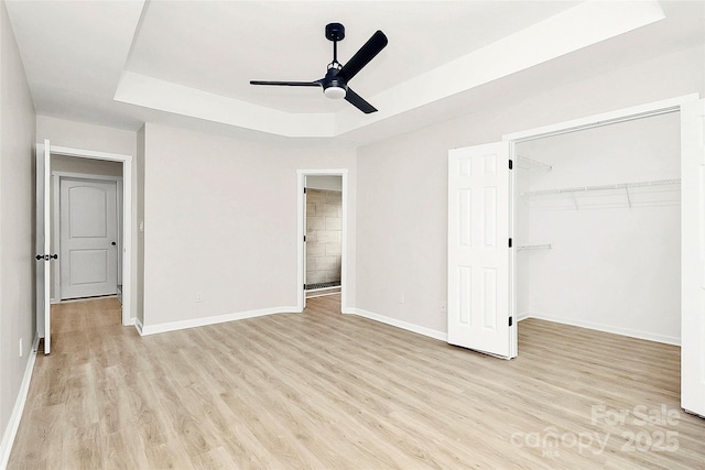 unfurnished bedroom with light wood finished floors, a closet, a raised ceiling, and baseboards