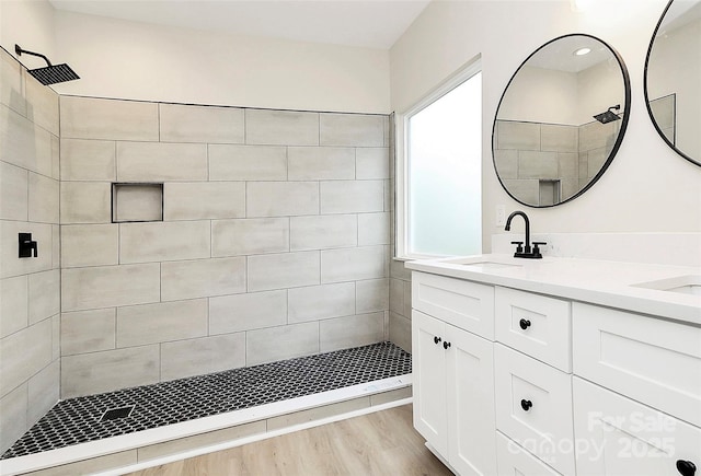 bathroom with a sink, tiled shower, wood finished floors, and double vanity