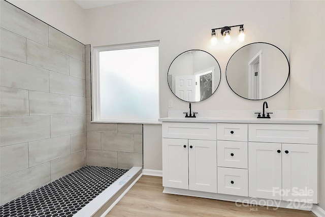 full bath with a sink, wood finished floors, double vanity, and a tile shower