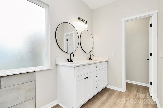 full bath featuring double vanity, wood finished floors, baseboards, and a sink