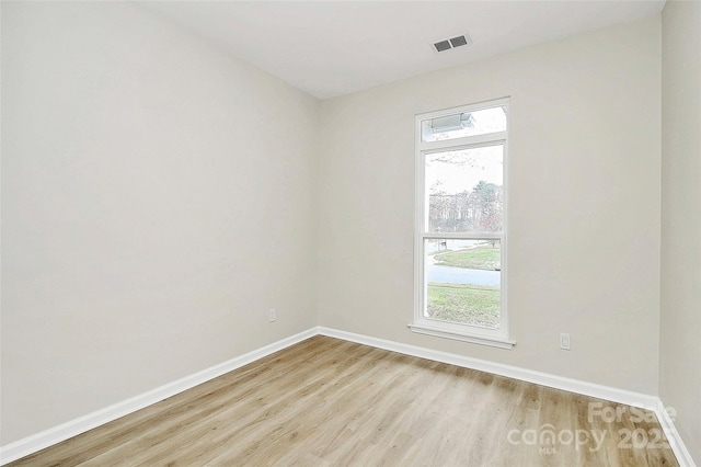 empty room with baseboards, visible vents, and light wood finished floors