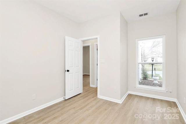 empty room featuring light wood finished floors, visible vents, and baseboards