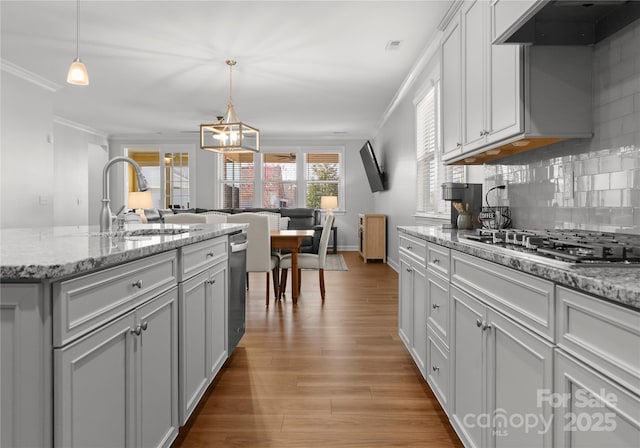 kitchen featuring wood finished floors, ornamental molding, stainless steel appliances, a sink, and under cabinet range hood