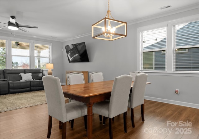 dining area featuring light wood finished floors, visible vents, crown molding, baseboards, and ceiling fan with notable chandelier