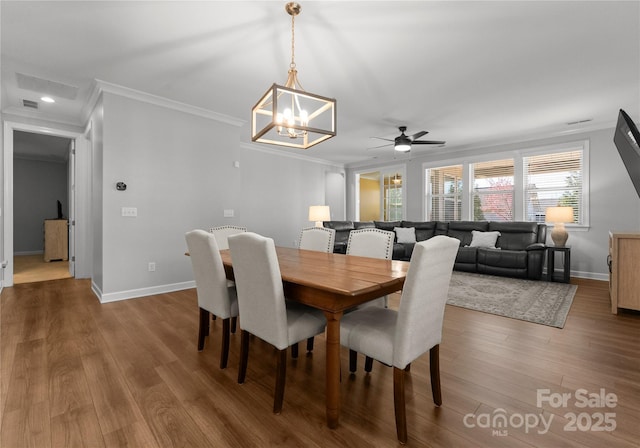 dining room featuring visible vents, baseboards, ornamental molding, ceiling fan with notable chandelier, and wood finished floors