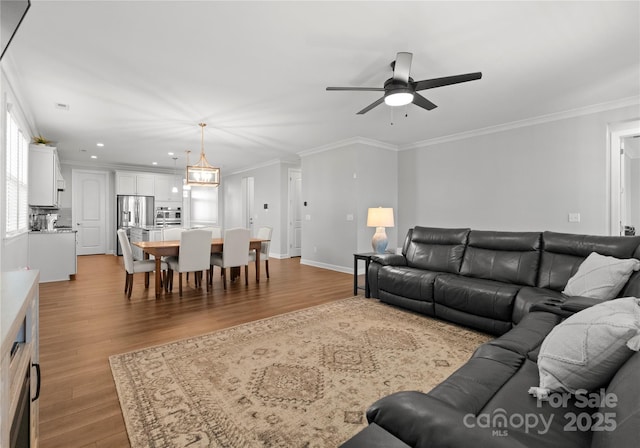 living area with baseboards, wood finished floors, a ceiling fan, and ornamental molding