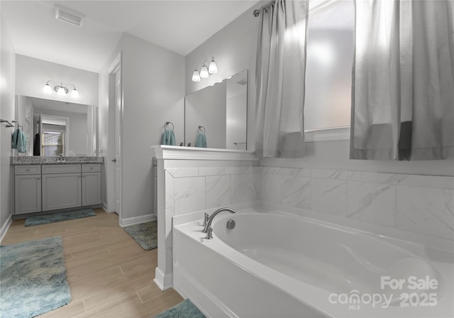 full bath with vanity, baseboards, visible vents, wood tiled floor, and a bath