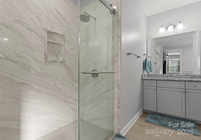 full bath featuring a marble finish shower, baseboards, wood finished floors, and vanity