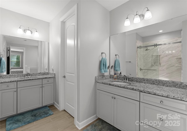 full bathroom with wood finish floors, two vanities, a marble finish shower, and a sink