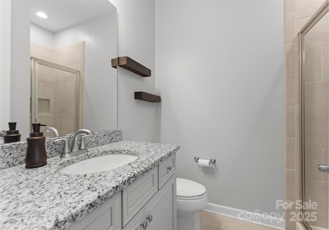 bathroom with vanity, a shower stall, toilet, and baseboards