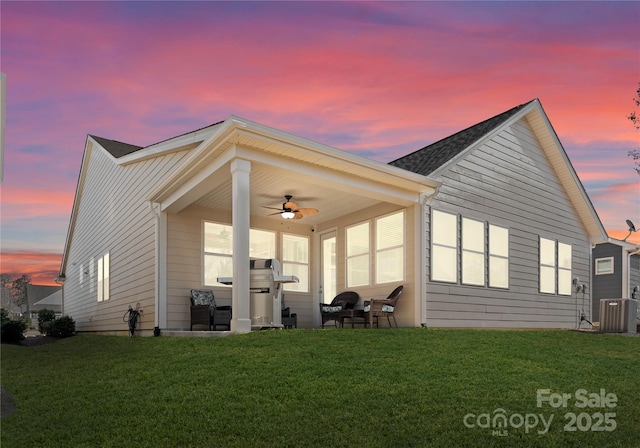 back of house at dusk with a lawn and ceiling fan