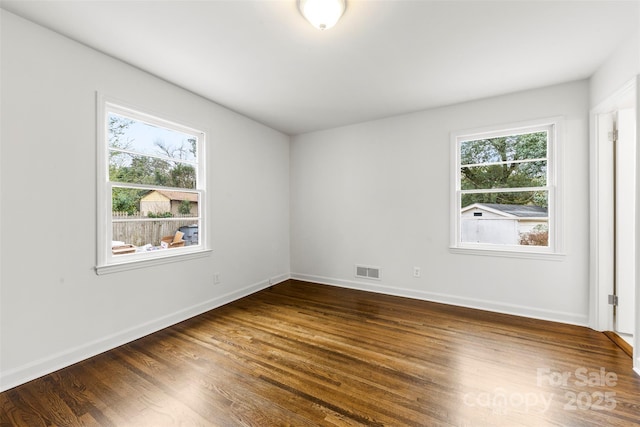 unfurnished room with a healthy amount of sunlight, baseboards, visible vents, and dark wood-type flooring