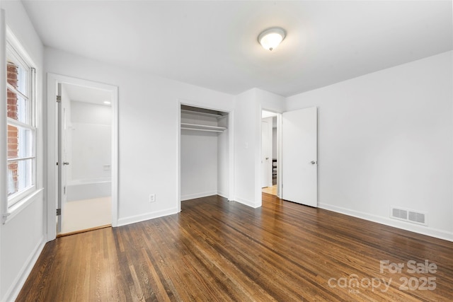 unfurnished bedroom featuring a closet, visible vents, dark wood-type flooring, ensuite bath, and baseboards