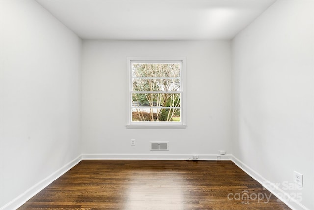 empty room with baseboards, visible vents, and dark wood-type flooring